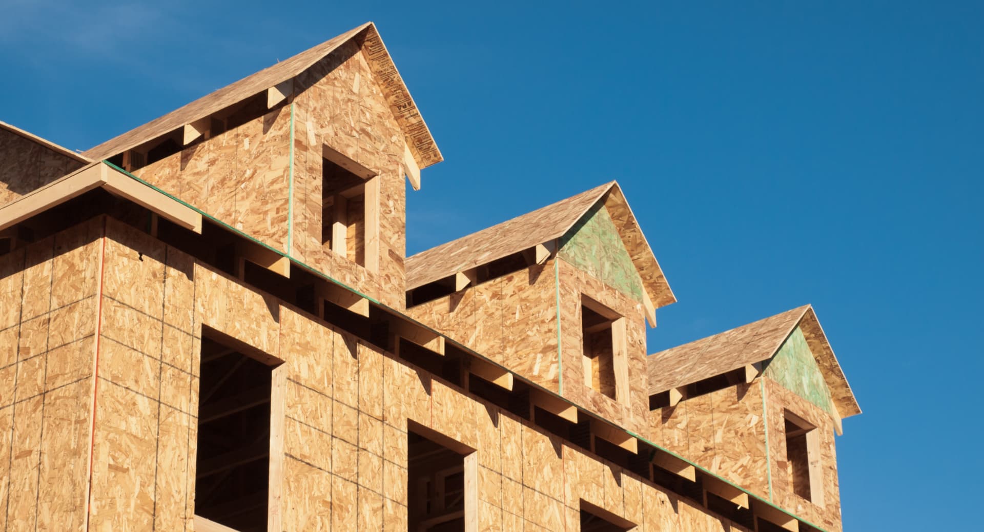 New homes under construction, framed walls and roof trusses against a clear blue sky.